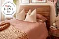 Cozy bedroom featuring a wooden headboard, pink linen bedding, large pillows, and a braided throw blanket.