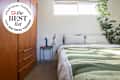 Cozy bedroom featuring a green and white striped quilt, wooden dresser, and a small bedside table with a blue lamp.