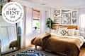 Cozy bedroom featuring a wooden bed frame, patterned quilt, decorative pillows, and a large plant by the window.