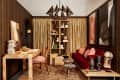 modern archival style room with yellow floral long curtains, deep red velvet sofa, artifacts, a desk, abstract art prints