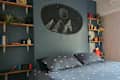 Bedroom with blue walls, mountain mural, geometric bedding, and wooden shelves with books and plants.