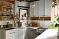 Modern kitchen with white cabinets, open wooden shelves, coffee machine, toaster, and potted plants by the window.