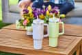 Two Stanley tumblers on a wooden table with a colorful flower arrangement in the background.