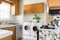 Kitchen with wooden cabinets, a dishwasher, stove with kettle, and a laundry area with washer, dryer, and potted plant.
