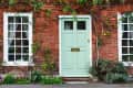 Mint green door on a red brick house with white-framed windows and climbing plants.