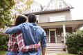 Couple embracing while looking at a two-story house with a porch.