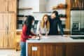 Three people reviewing documents at a kitchen island with wooden cabinets and modern appliances.