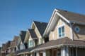 Row of suburban houses with gabled roofs and varied siding colors under a clear blue sky.