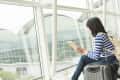 Woman in striped shirt sitting by airport window with suitcase, reading a map.