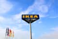 IKEA sign on a tall pole against a blue sky with flags below.
