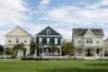 Three suburban houses with picket fences, one yellow, one blue, and one cream, on a grassy street.