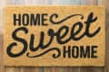 Brown doormat with "Home Sweet Home" in black script on wooden floor.