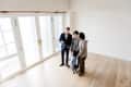Real estate agent showing an empty room with wooden floors to a family of three.
