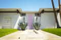 Mid-century modern house with a pink door, agave plants, and manicured lawn under a clear blue sky.