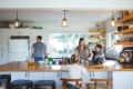 Family in a kitchen with wooden countertops, pendant lights, and open shelves. A child sits on the counter.