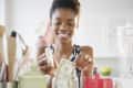 Woman smiling while placing dollar bills into a jar in a kitchen setting.