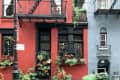 Red brick building with black fire escape, potted plants, and window boxes filled with greenery and flowers.