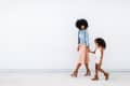 Woman in denim jacket and pleated skirt walking with a young girl in a floral dress and boots.