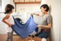 Mother and daughter folding a blue towel in a laundry room with a washing machine.