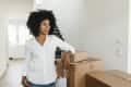 Woman in white shirt leaning on stacked moving boxes in a bright hallway.