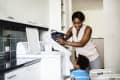 Woman doing laundry with a child in a modern laundry room, smiling while loading clothes into a washing machine.