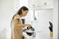 Woman pouring coffee into a mug in a bright kitchen with white cabinets and a knife block.