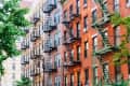 Red brick apartment buildings with black and green fire escapes and trees in the foreground.