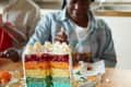 Multi colored cake on table while teenage girl sitting in background during birthday party