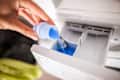 Someone pouring liquid detergent into laundry machine.