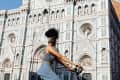 Young woman riding bicycle in front of cathedral, Florence, Italy