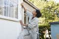 Woman repairing the outdoor window trim on her house