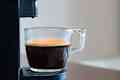 Close up of refreshing espresso pouring of capsule machine into a cup at home. Concept of coffee break.