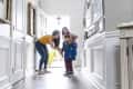 Mother getting 2 children ready for school in front doorway, each kid has a backpack
