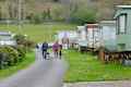 Couple walking their dogs around a caravan site with static caravans parked either side on a Spring day enjoying a vacation in rural Wales UK.