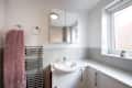 A general view of a small white bathroom with grey wall tiles, toilet, bathtub, medicine cabinet. Sink mounted to a vanity unit with chrome taps