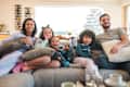 Indoor shot of multiracial family relaxing. Front view of them watching tv while holding on cushions.