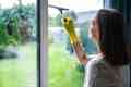 A woman cleaning window pane of country house with a squeegee