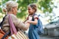 A touching moment as a mother helps her daughter get ready for school, embodying care, love, and support. Outdoors, highlighted by warm morning light and a cheerful atmosphere, this image captures family togetherness.