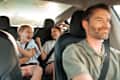 Smiling dad driving car with 2 girls in the back laughing