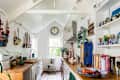 Galley style white kitchen with pitched roof, wooden worktops and open shelving. The walls are adorned with boats made by Rachel Sumner from recycled wood and found materials.