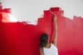 Rear view of girl painting red wall with paint roller