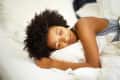 Woman with curly hair sleeping peacefully on white bedding.
