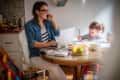 Mom working on computer at the kitchen table while toddler daughter colors