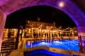Nighttime outdoor event at a villa with string lights, guests mingling by a lit pool under an arched entrance.