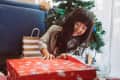Child opening a gift in front of a christmas tree. Other gifts and blue sofa in background
