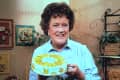 Julia Child in her kitchen with a cake in hand.