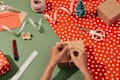 hands wrapping gift, red and white wrapping paper on green surface, scissors, twine