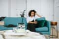 Woman sitting on a teal sofa using a smartphone, with a teapot and books on a tray in front.