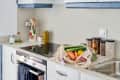 Modern kitchen with induction stove, utensils, jars of spices, and a mesh bag of fresh vegetables on the counter.