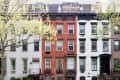 Three-story brownstone buildings with red brick and white facades, framed by trees.